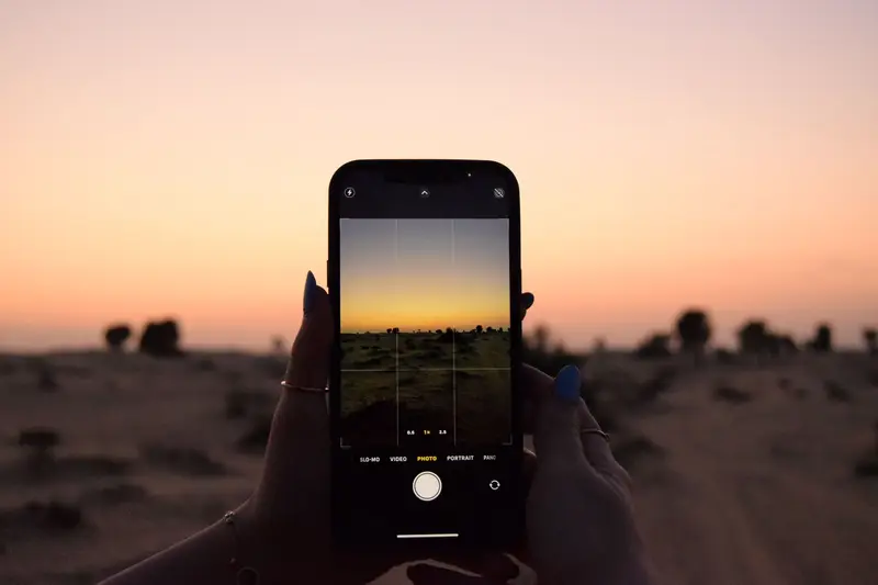 A smartphone resting in the shade of a backpack on a hiking trail with saguaro cactus and bright desert sun in the background